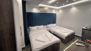 A hotel room with two beds, a blue headboard, a small desk with a vase of flowers, and recessed ceiling lighting. - Premier Pyramids Inn (Giza)