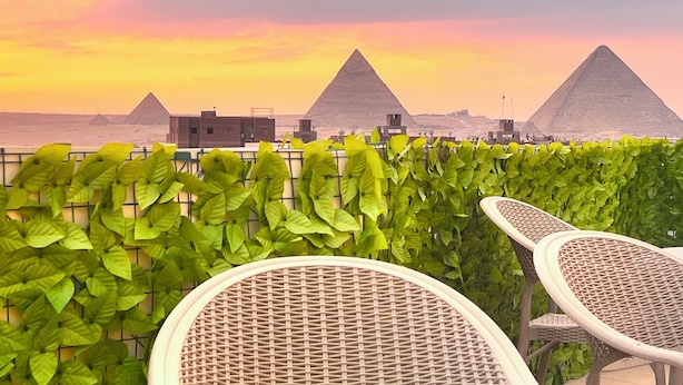 A view of the pyramids at sunset with a green hedge and wicker chairs in the foreground. - Premier Pyramids Inn (Giza)