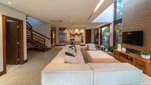 A spacious living area with a sofa set, a TV mounted on the wall, and a staircase leading to another level.