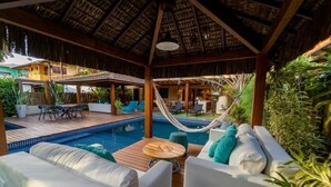 A poolside area with a hammock, white sofas, and a wooden deck.