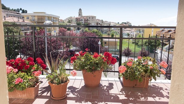 En balkon med plantekasser og udsigt over en by med bygninger og et tårn.