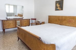 Un dormitorio con cama, cómoda, espejo, silla, lámpara y un cuadro en la pared.