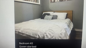 Een queensize bed in een slaapkamer, met een spiegel erboven en drie ingelijste kunstwerken aan de muur.