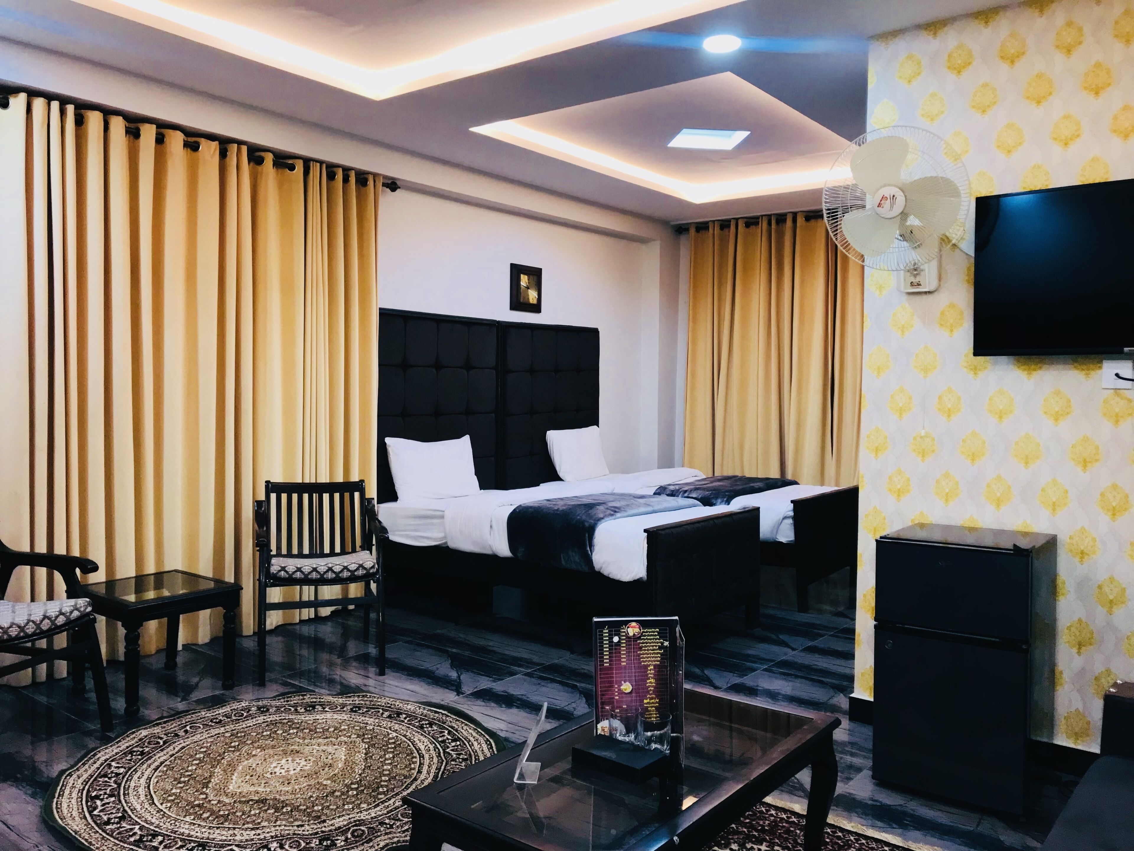 A hotel room with a bed, a desk, a chair, a TV, and a fan.