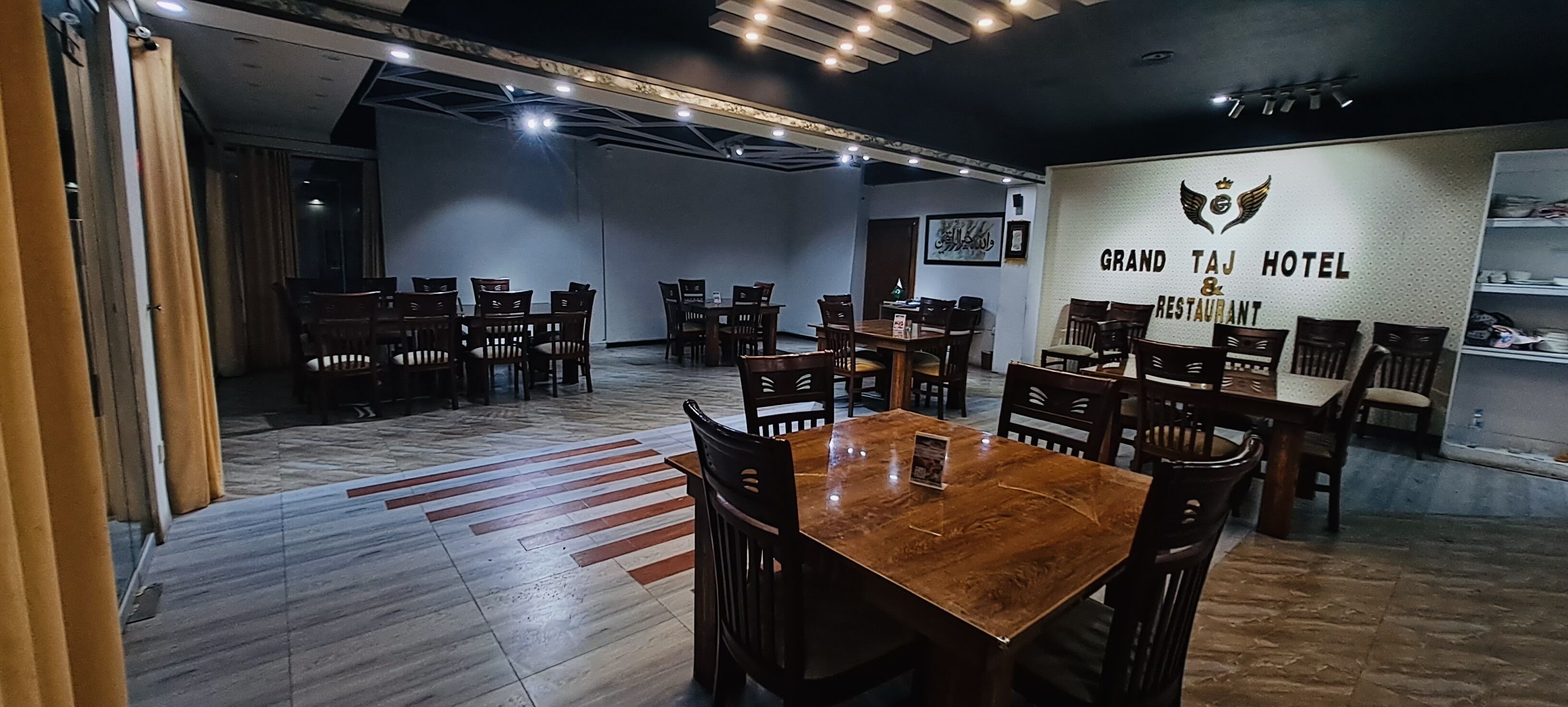A spacious dining area with multiple wooden tables and chairs, a polished floor, and a wall with the hotel name.