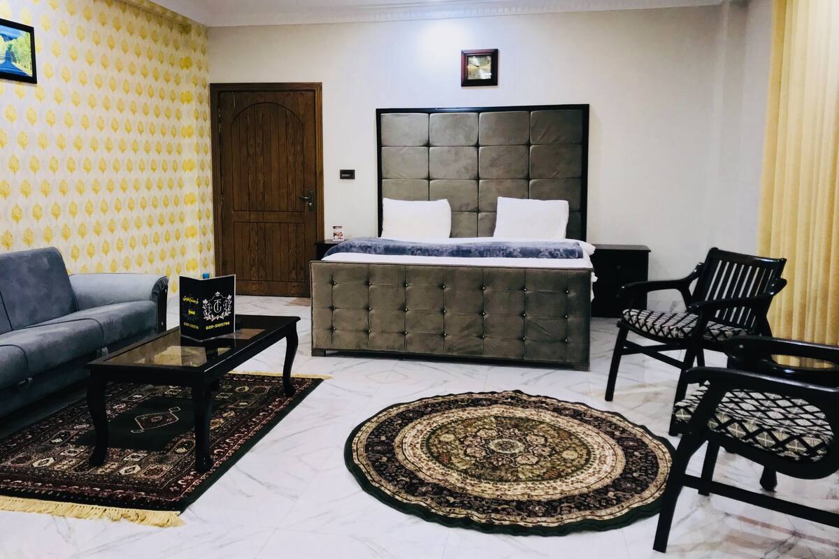 Ein Hotelzimmer mit Bett, Sofa, Couchtisch, zwei Stühlen, Teppich und einer Tür.