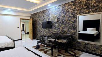 A hotel room with two beds, a seating area with chairs, a TV mounted on the wall, and a large mirror.
