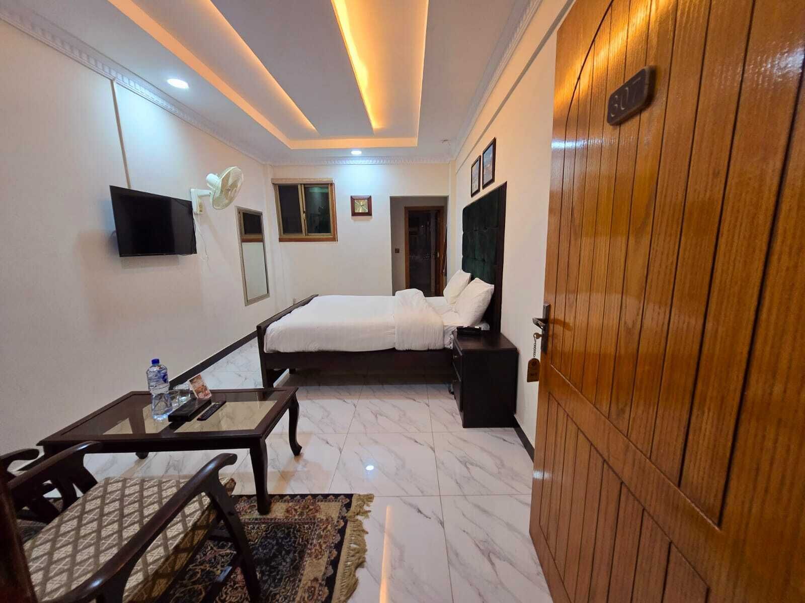 Una habitación de hotel con cama, mesita de noche, silla y televisor montado en la pared.