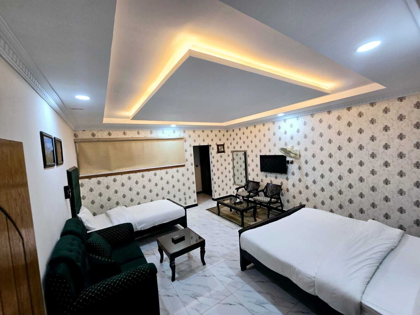 A hotel room with two beds, a sofa, a small table, a TV, and a mirror.