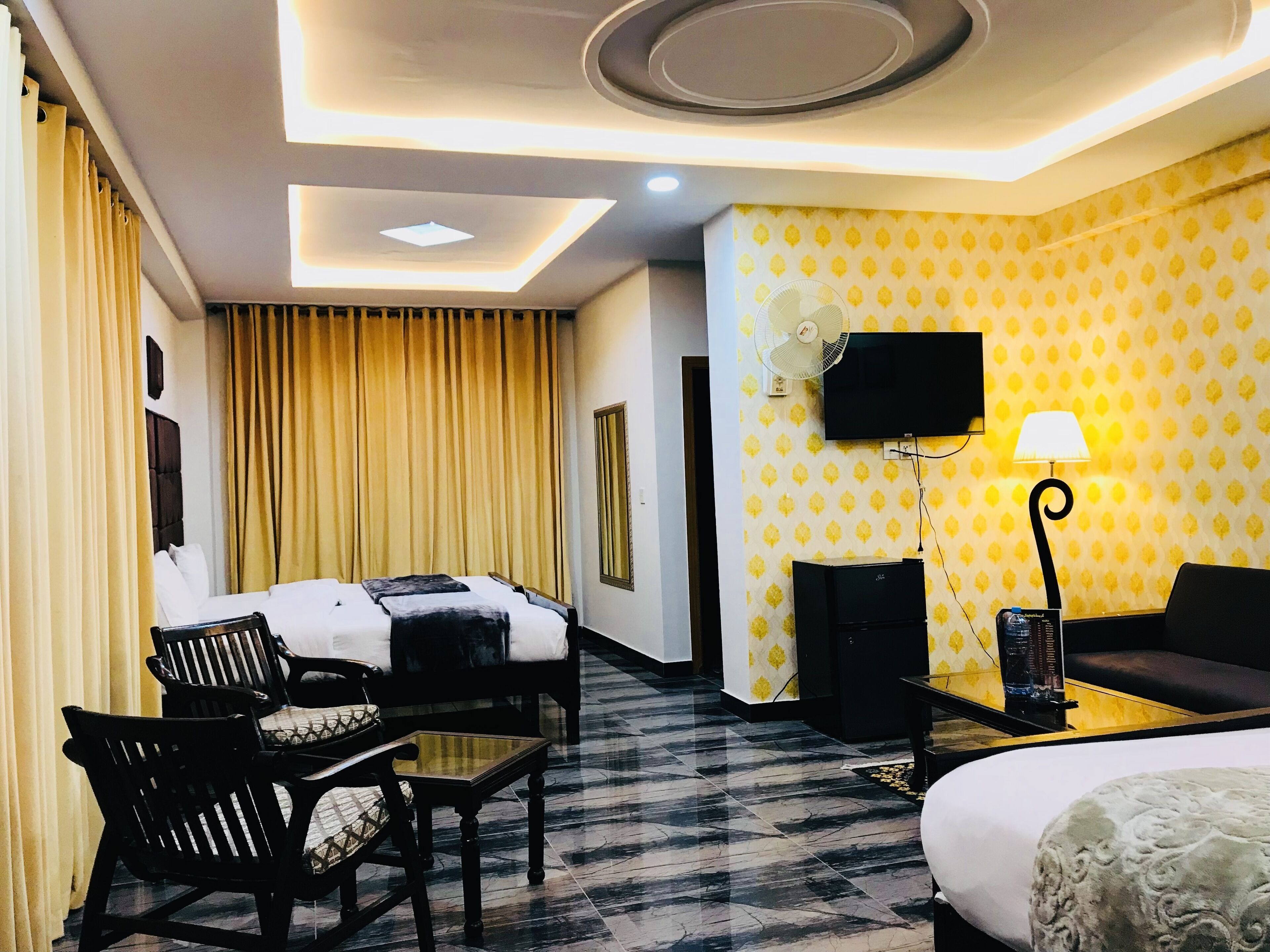 A hotel room with a bed, a desk, a chair, a sofa, a TV mounted on the wall, and a lamp.