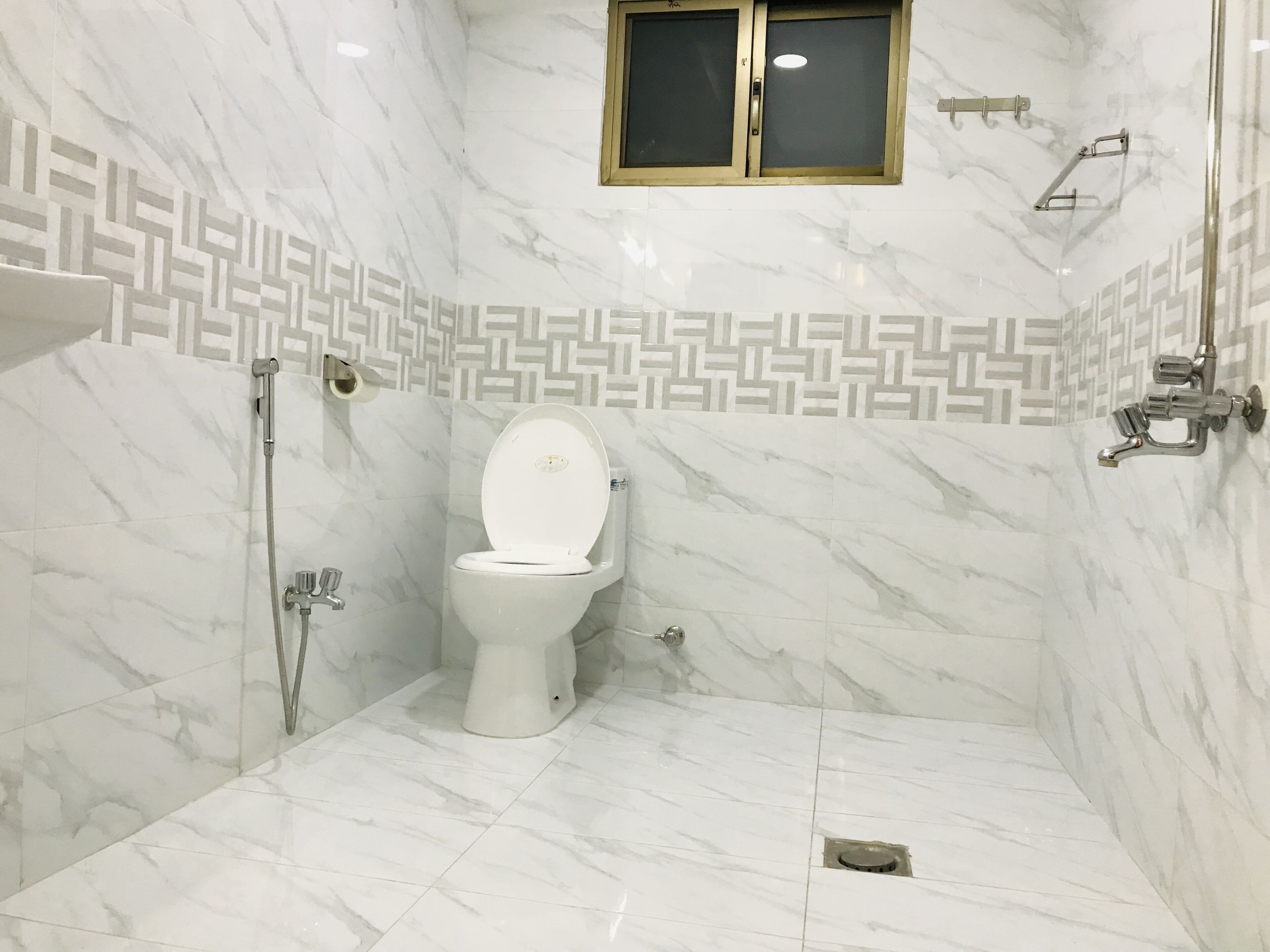 A bathroom with a toilet, shower, and a window.