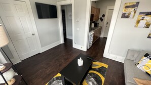 Un salon moderne avec une table basse noire, un canapé gris et une cuisine en arrière-plan.