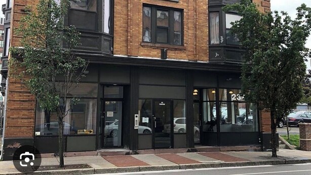 Un immeuble d’angle avec une façade en briques, de grandes fenêtres et un auvent noir.