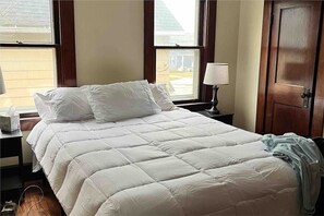A bedroom with a large bed, a nightstand with a lamp, and a door. - River House on BW campus! (Berea)