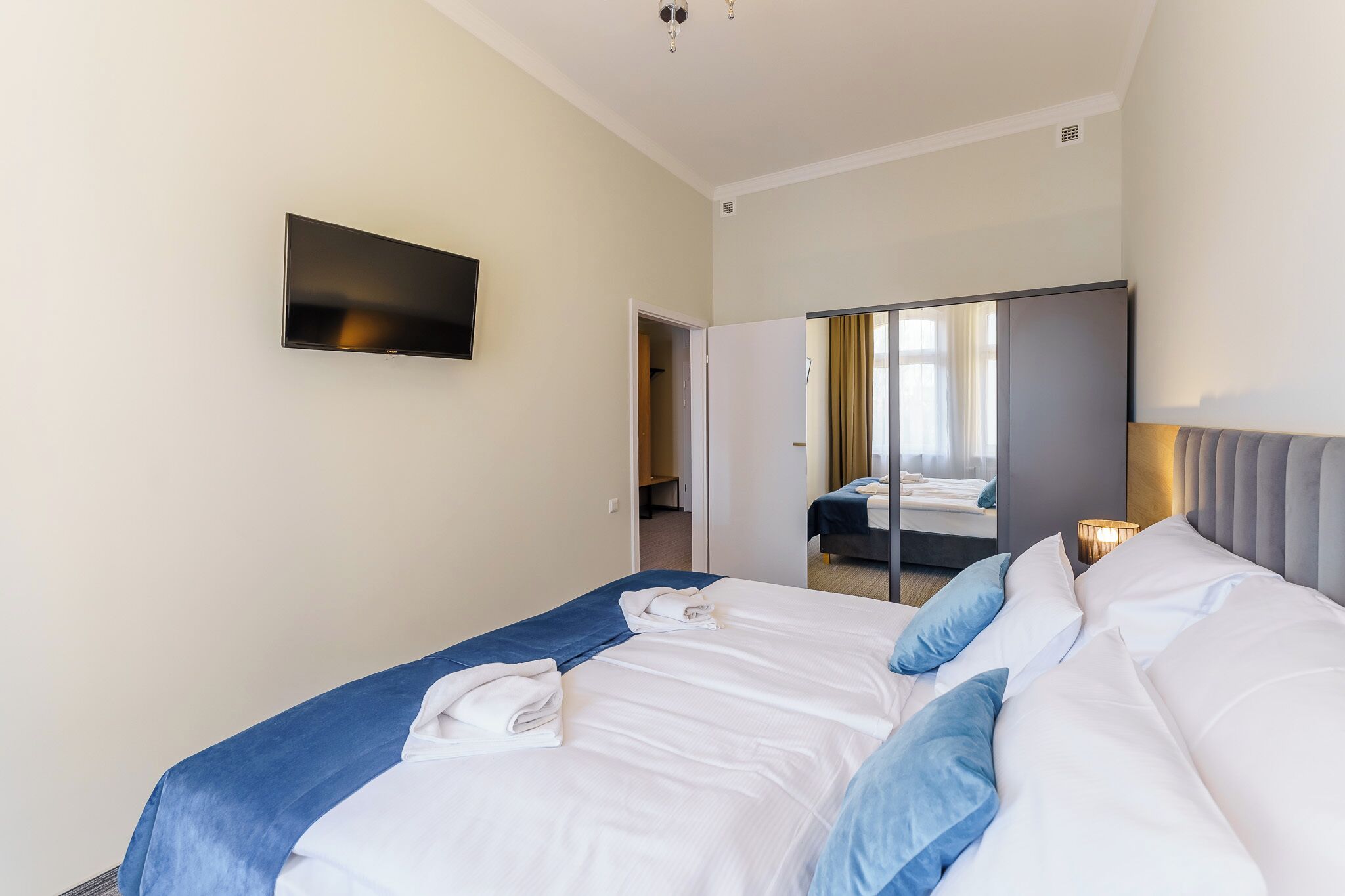 A hotel room with a large bed, a flat-screen TV mounted on the wall, a wardrobe, and a mirror.
