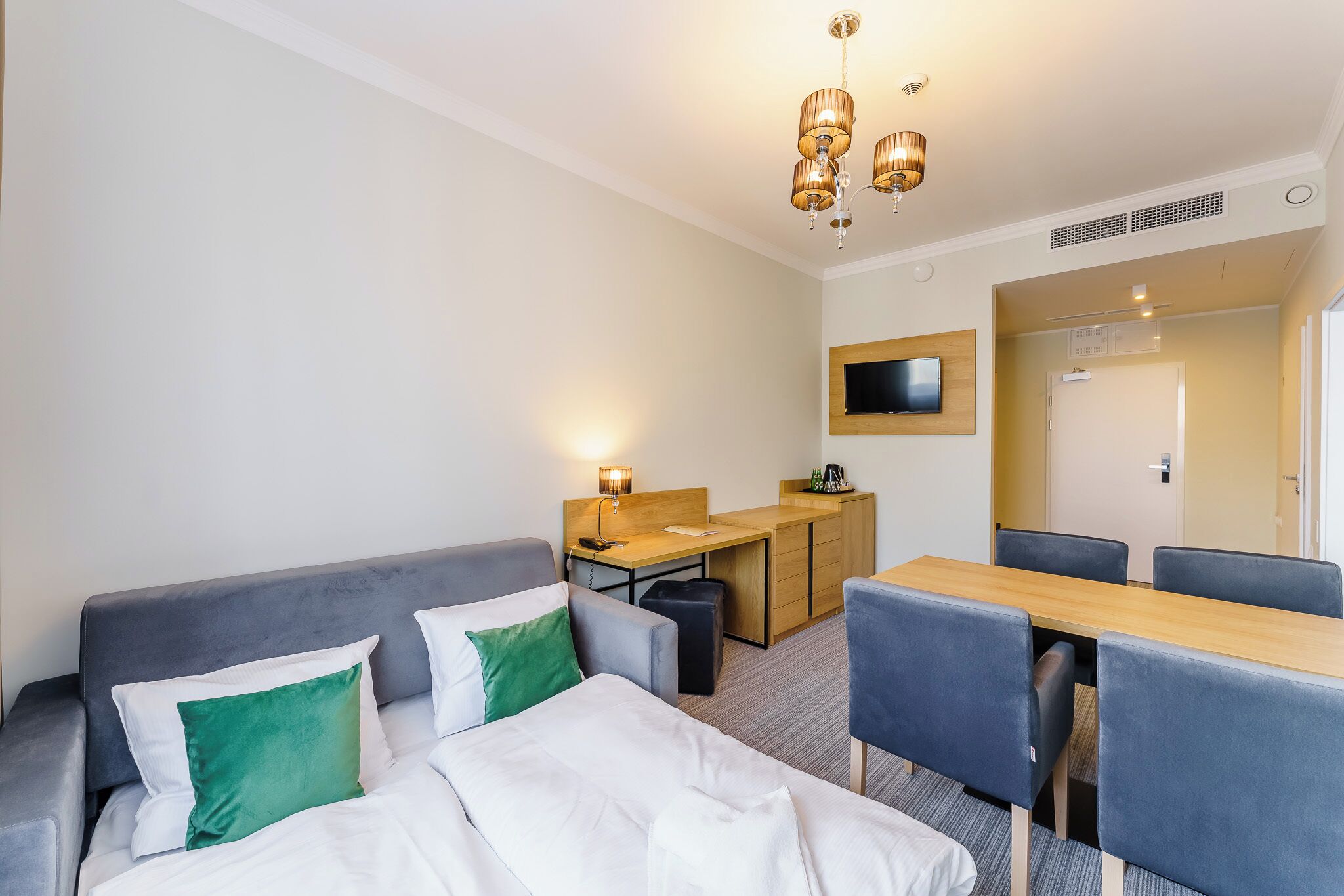 Una habitación de hotel con una cama, un sofá gris, un escritorio de madera y una mesa de comedor con sillas.