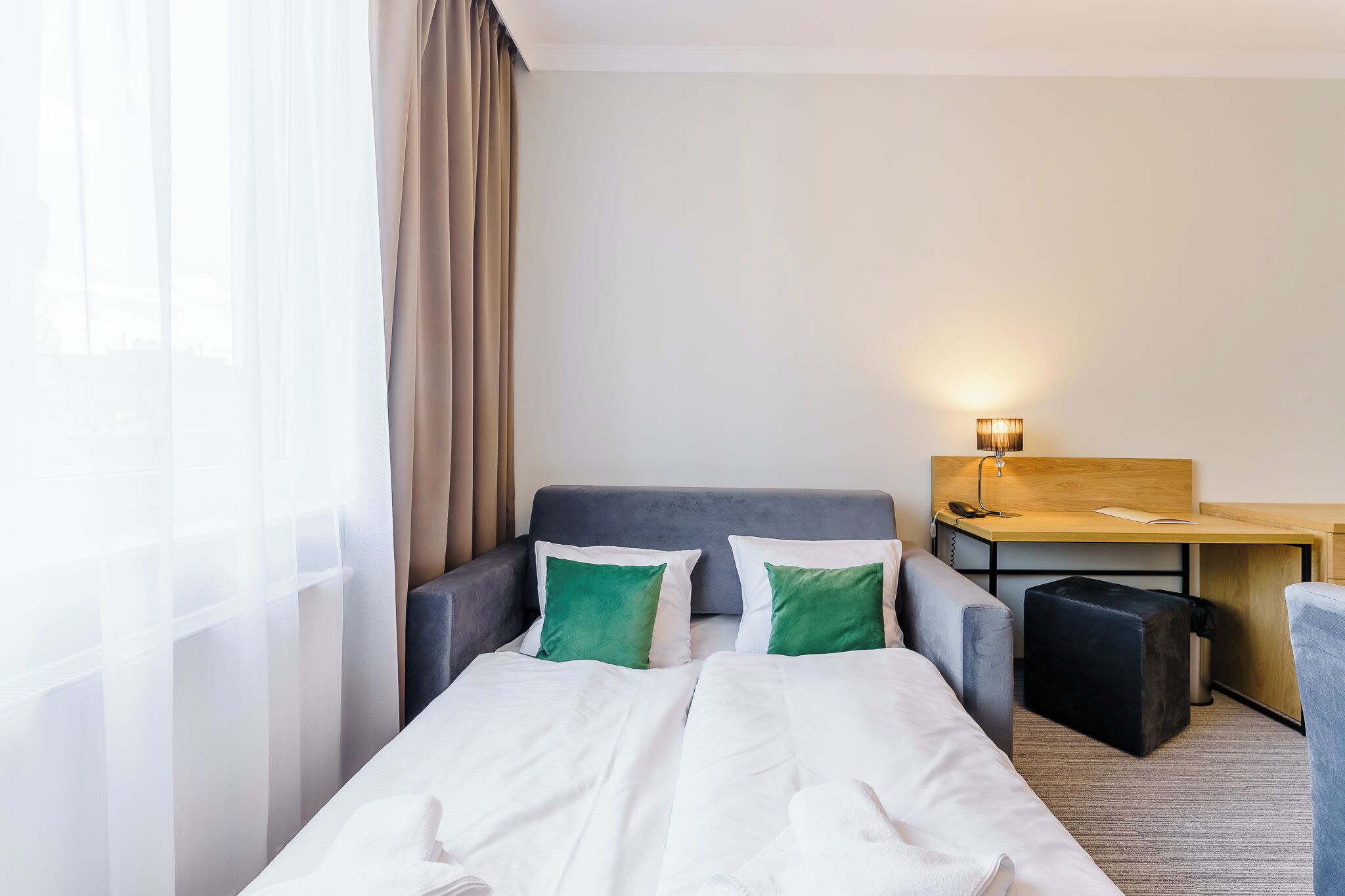 Una habitación de hotel con cama, escritorio, silla y un taburete pequeño.