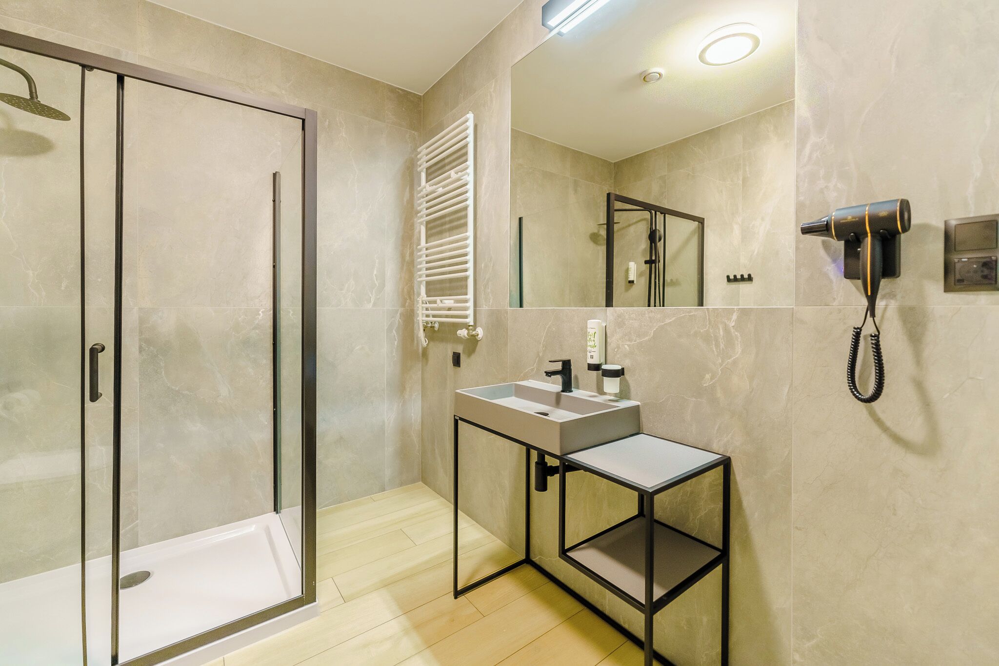 A modern bathroom with a glass shower enclosure, a vanity with a sink, and a hairdryer mounted on the wall.