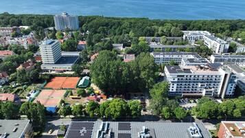 Vista aérea de una zona urbana costera con varios edificios, incluyendo un hotel grande con múltiples pisos y una terraza en la azotea.