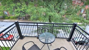 A balcony with a glass table and two chairs, overlooking a parking area and a building with trees. - Luxury 2 bedroom, 2 bath condo , 2 balconies, hi speed WIFI with FREE parking (Montréal)