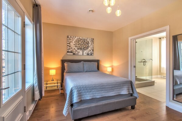 Ein Schlafzimmer mit einem großen Bett, Nachttischlampen, einer Glasdusche und Blick ins Freie.