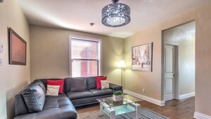 A living room with a black leather sectional sofa, a glass coffee table, a lamp, and a door leading to another room. - Luxury 2 bedroom, 2 bath condo , 2 balconies, hi speed WIFI with FREE parking (Montréal)