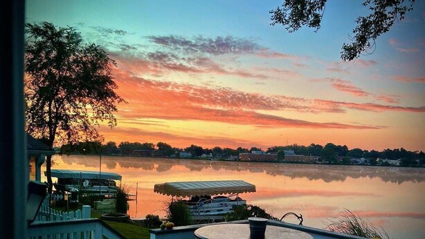 A lakeside view with a gazebo, a round table, and a white picket fence.