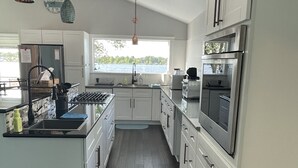 A modern kitchen with white cabinets, stainless steel appliances, and a large window overlooking a lake.