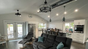 A modern kitchen with white cabinets, stainless steel appliances, and a dining area with a gray sofa and chairs.