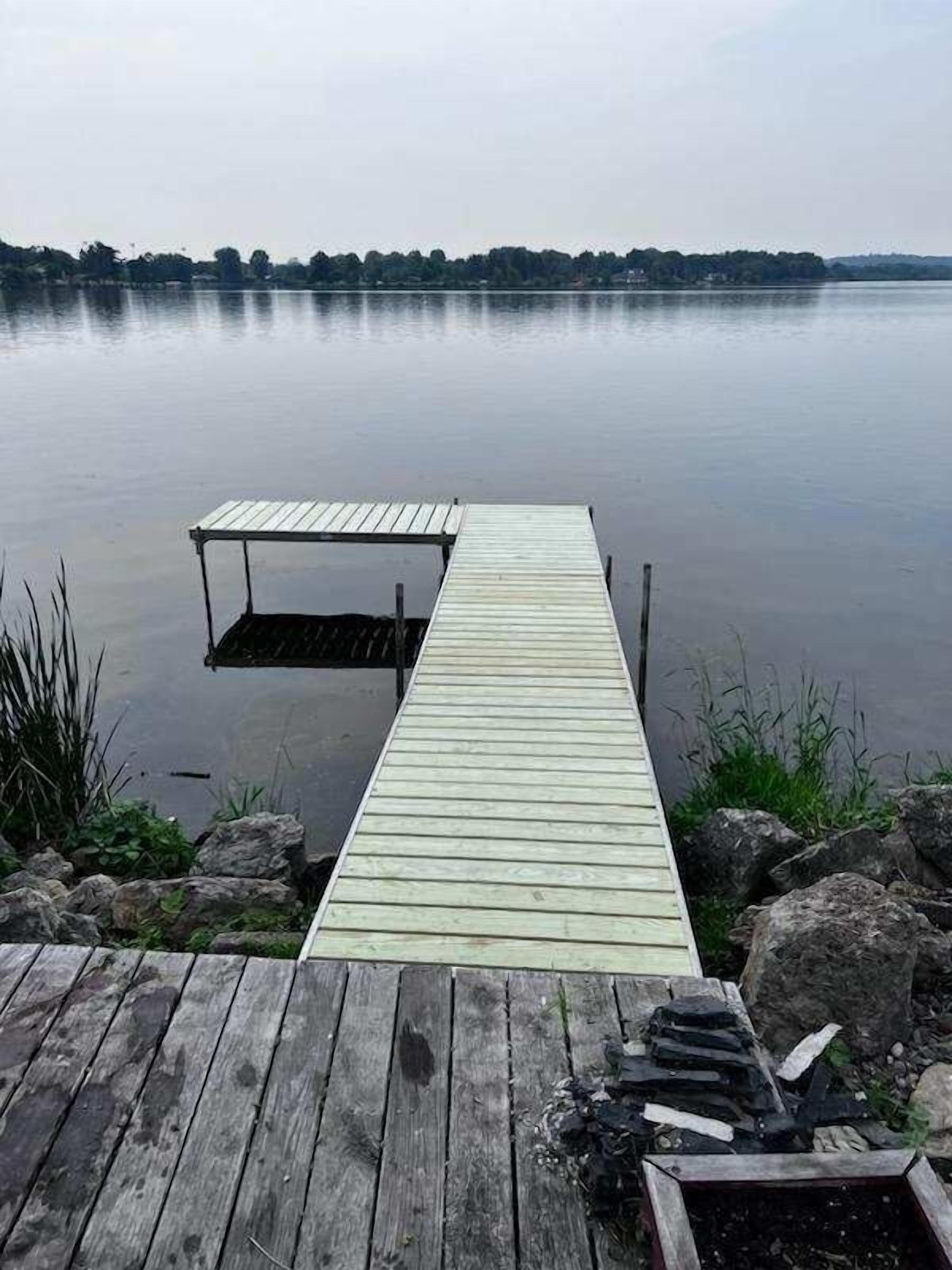Une jetée en bois s’étendant dans une étendue d’eau calme, entourée de rochers et de végétation.