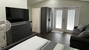A modern bedroom with a bed, a TV, a dresser, a fan, and a sliding glass door leading to a balcony.