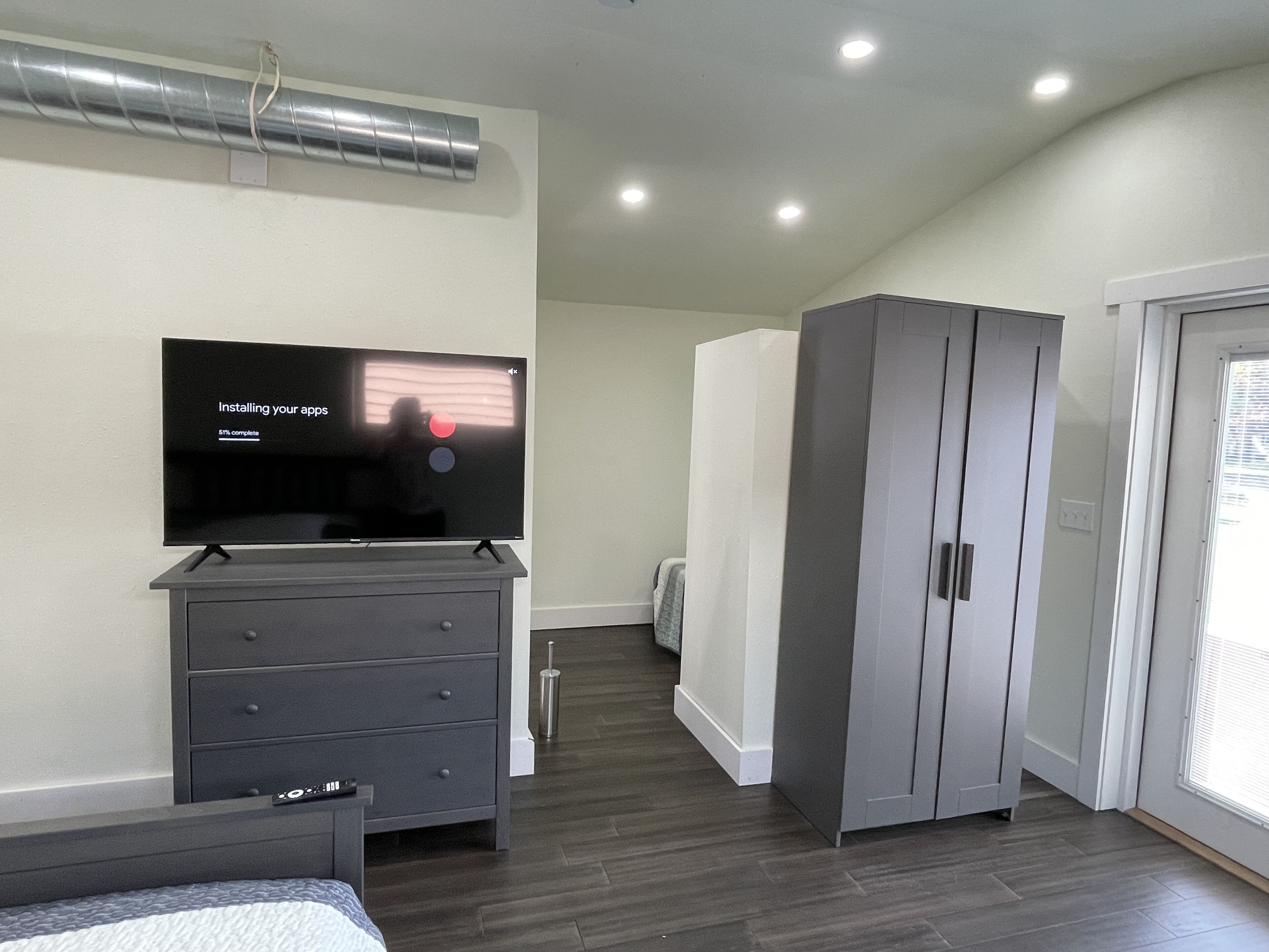 A modern bedroom with a flat-screen TV on a dresser, a wardrobe, and a bed.