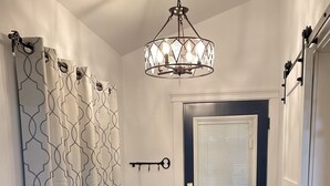 A hallway with black tiled flooring, a grey rug, a decorative key hanging on the wall, and a ceiling light fixture.