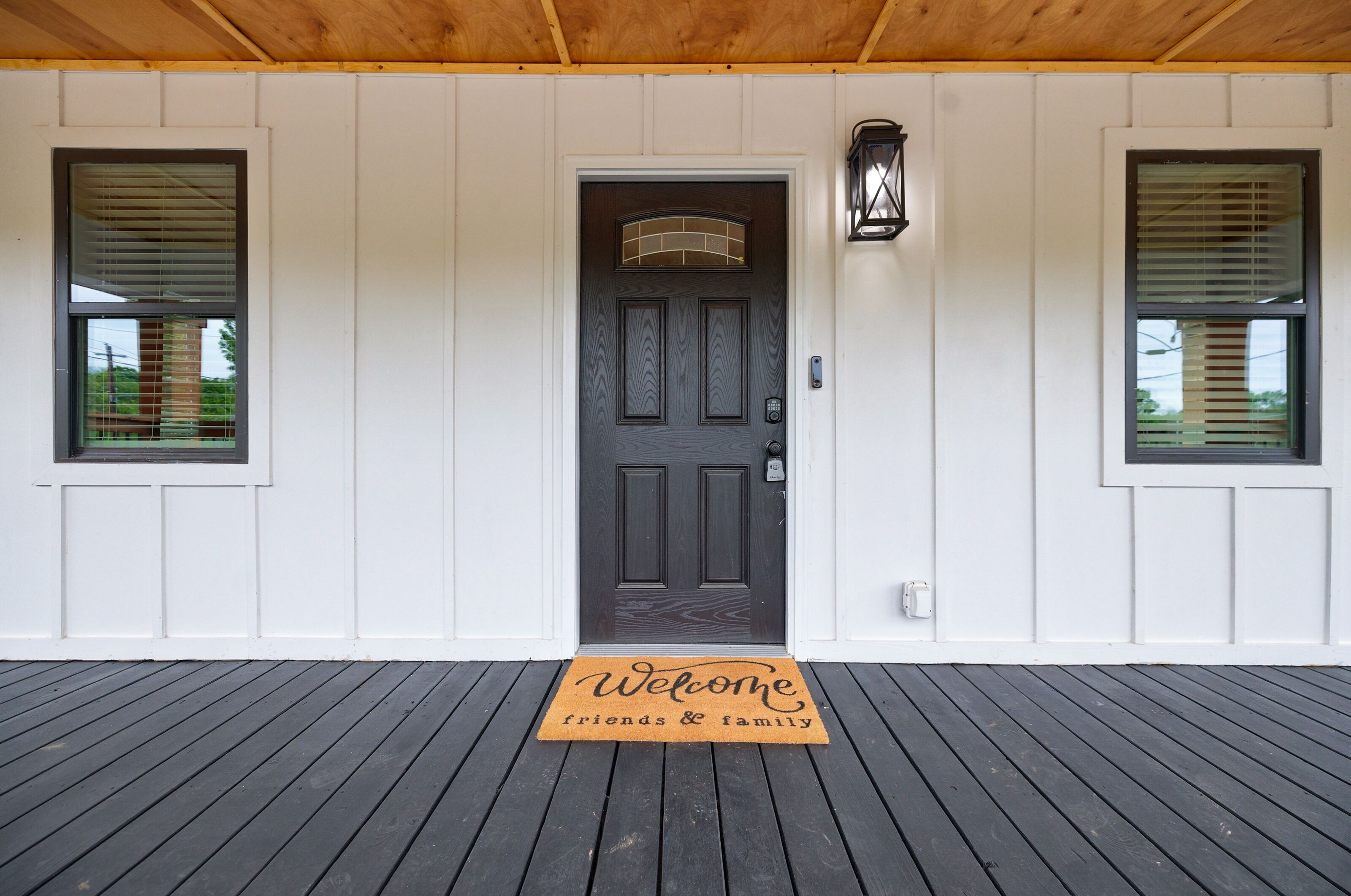 A wooden deck with a dark door and a welcome mat.