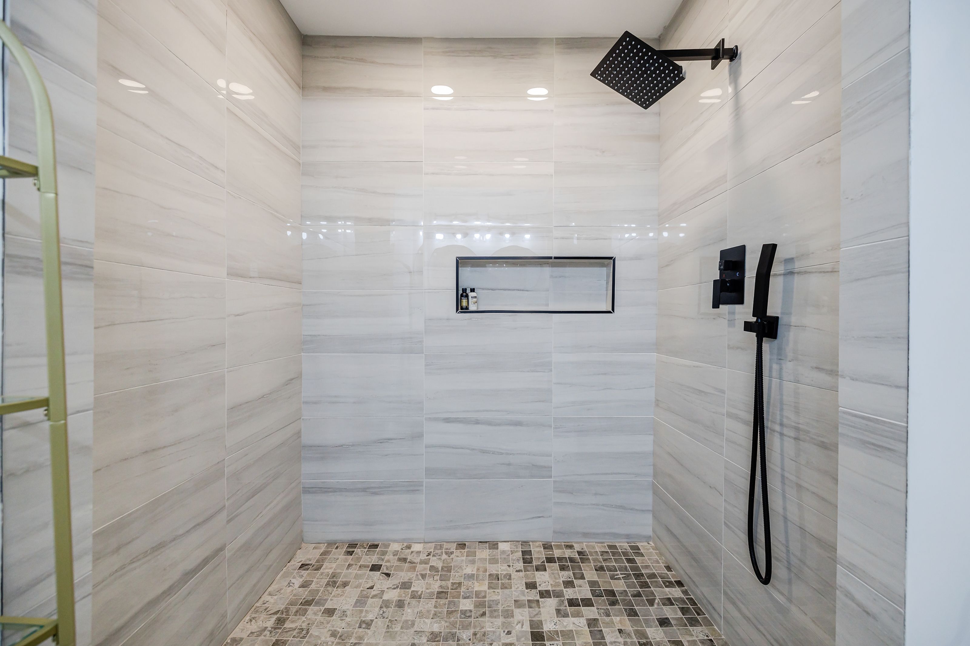 A modern shower with a tiled floor, a wall-mounted control panel, and a handheld showerhead.