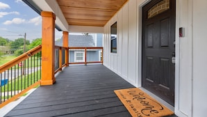 A covered porch with a dark wooden floor, a black door, and a welcome mat. - Atlanta's Hidden Gem: Modern 4BR/2BA House with Grill and Outdoor Space! (Atlanta)