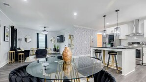 A modern kitchen with a central island, bar stools, and a round glass table with chairs. - Atlanta's Hidden Gem: Modern 4BR/2BA House with Grill and Outdoor Space! (Atlanta)