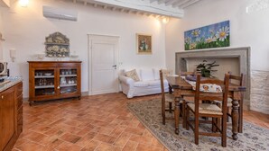 A cozy living room with a fireplace, a dining area with wooden chairs, a white sofa, and a tiled floor. - Tina's House (Cortona)