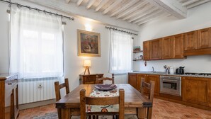 A dining area with a wooden table and chairs, a rug, and a kitchen with wooden cabinets and appliances. - Tina's House (Cortona)