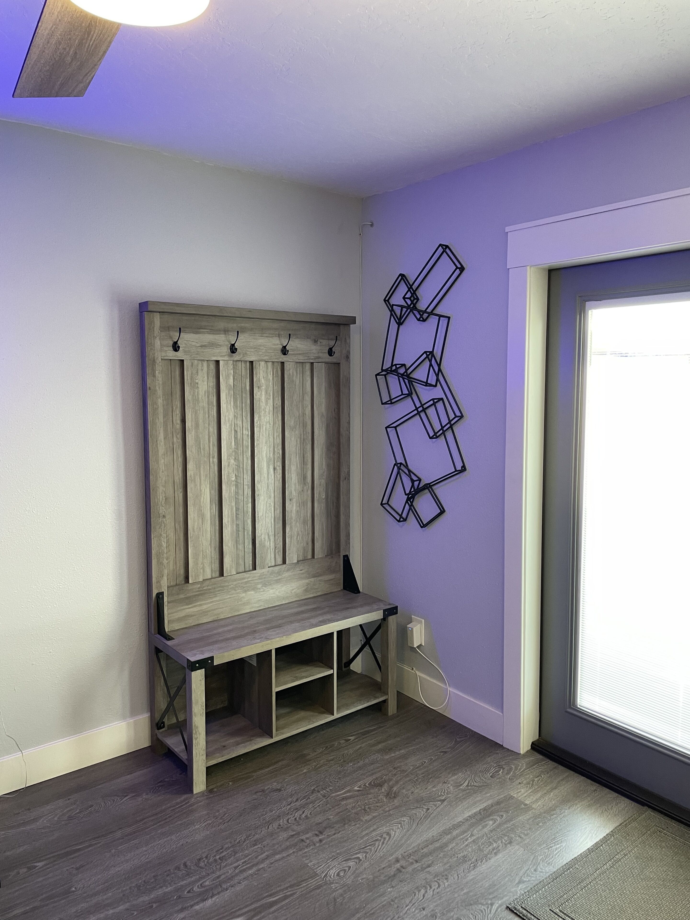 A room with a wooden bench, a wall-mounted geometric light fixture, and a window with blinds.