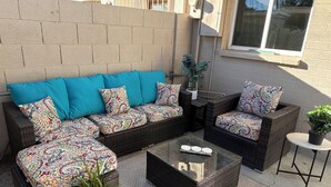 Eine Terrasse mit einer Rattan-Sitzgruppe, einem Glastisch und einem kleinen runden Tisch mit einem Blumentopf.