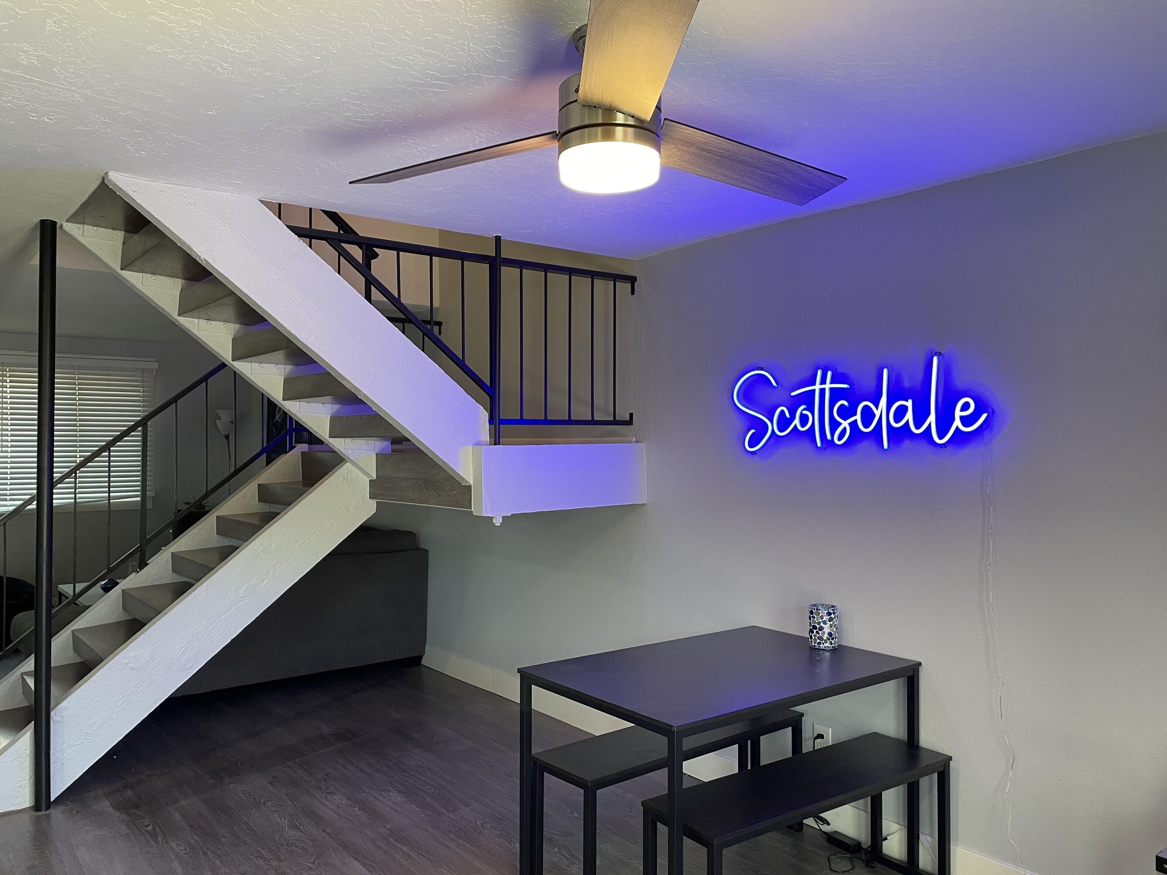 A modern interior with a staircase, a ceiling fan, and a neon sign on the wall.