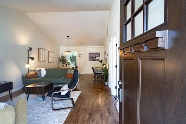 Relax in this spacious living area with a high ceiling and large window, featuring a green sofa, armchair, and dining area.