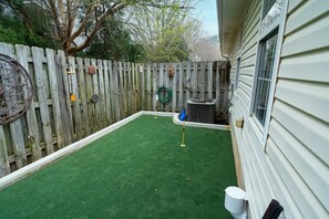 Backyard with artificial turf, enclosed by a fence, featuring a play area and outdoor water access.