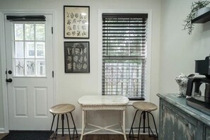 Cozy retreat with a wicker table and stools, a botanical print, and a potted plant.