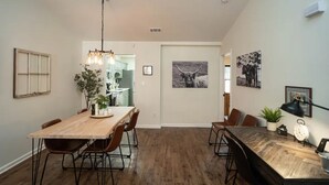 Un coin repas avec une table et des chaises en bois, un luminaire suspendu et des tableaux encadrés aux murs.