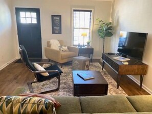 Relax in this inviting living room with a large flat-screen TV, comfortable sofa, and cozy armchair.