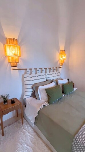 A bedroom with a bed, pillows, a nightstand, and wall-mounted lamps.