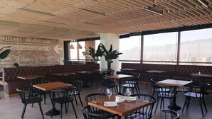 Un café moderno con paneles de techo de madera, arreglos de asientos y ventanas amplias que ofrecen vista a la ciudad.