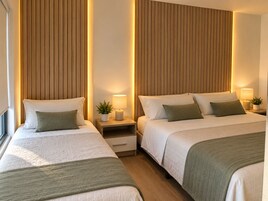 Habitación de hotel con dos camas, cabeceros de madera, mesitas de noche con lámparas y una pequeña planta en maceta.